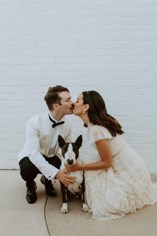 Bride and groom kneeling, embracing dog and kissing for Paulina & Cam’s Wedding