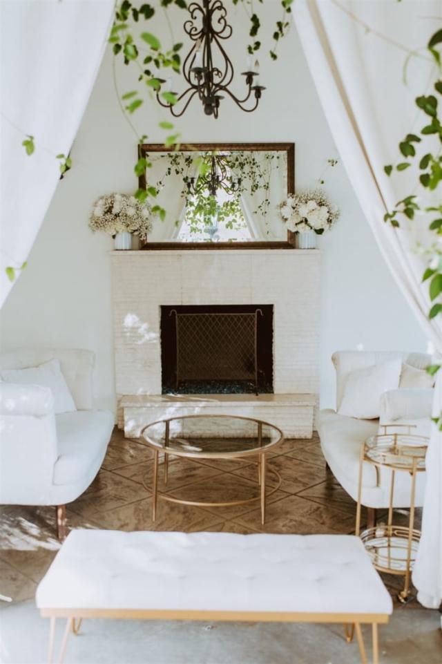 View through curtains of couches in front of fire place with mirror and flowers for Paulina & Cam’s Wedding