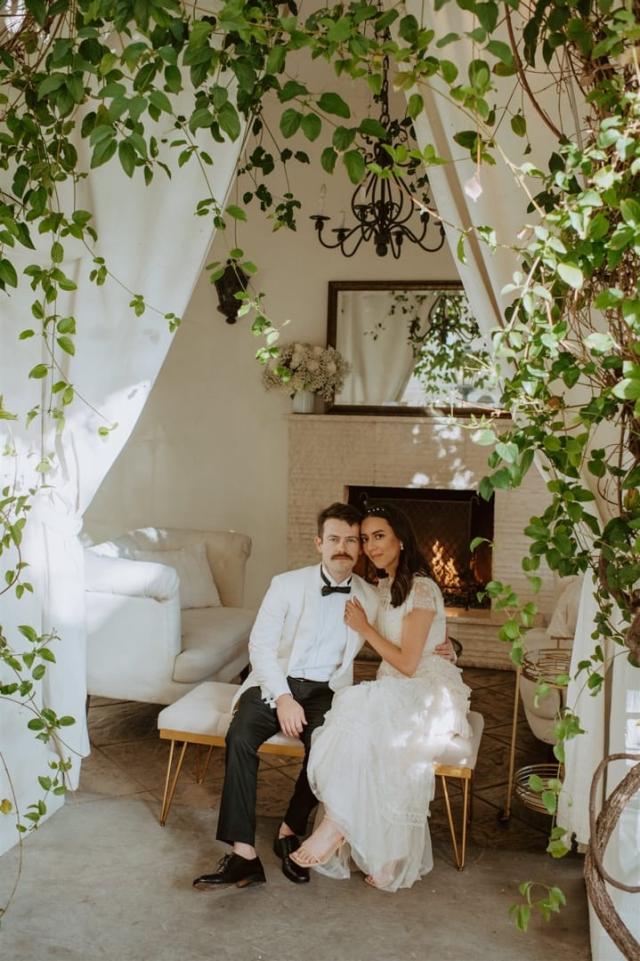 Bride and groom embracing on table between curtains and creepers for Paulina & Cam’s Wedding