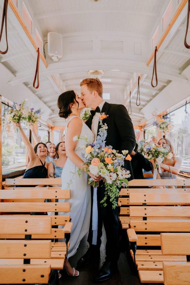 Bride and groom kissing on tram in front of wedding party for Veronica & Jake’s Wedding