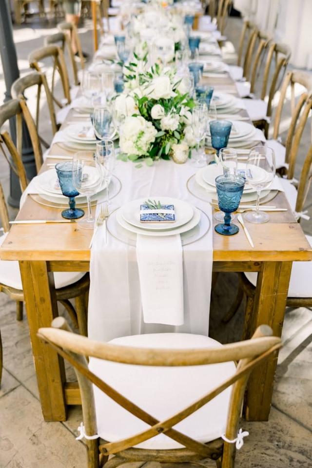 Long view of table with place sets, flowers, and blue glasses for Sara & James’ Wedding