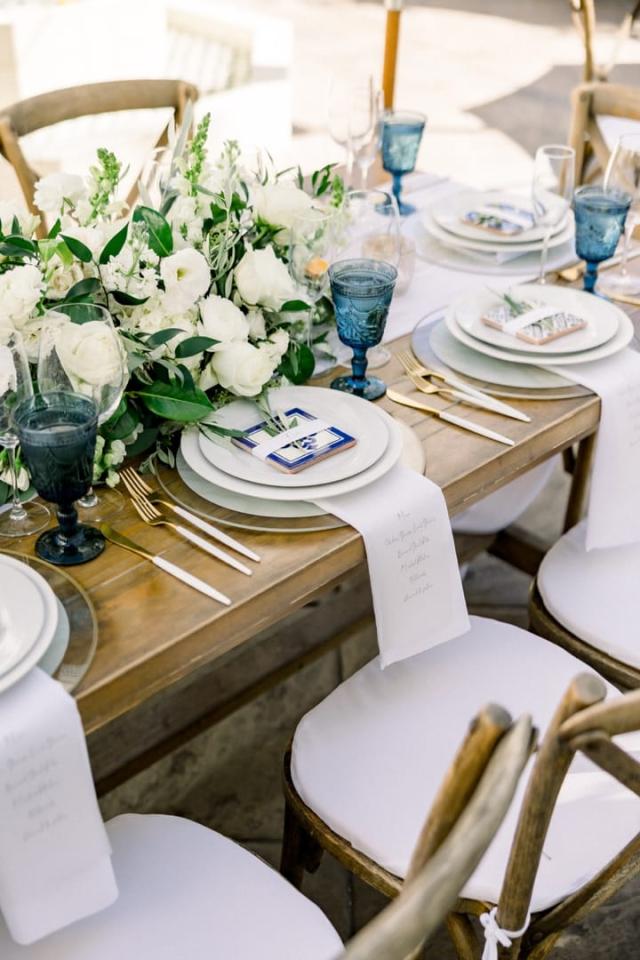 Close view of wedding table end with place sets, flowers, blue glasses and menus for Sara & James’ Wedding