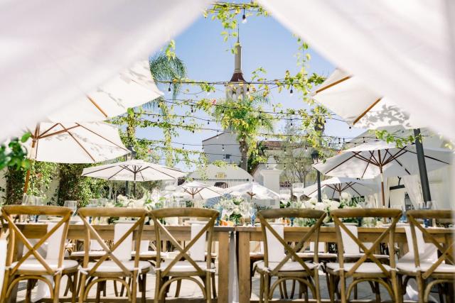 Low view of wedding tables, creepers, umbrellas, with chapel in the distance for Sara & James’ Wedding