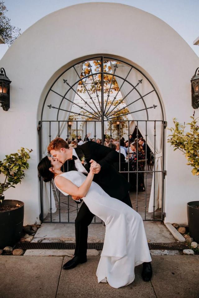 Groom dips bride in front of gate archway for Veronica & Jake’s Wedding