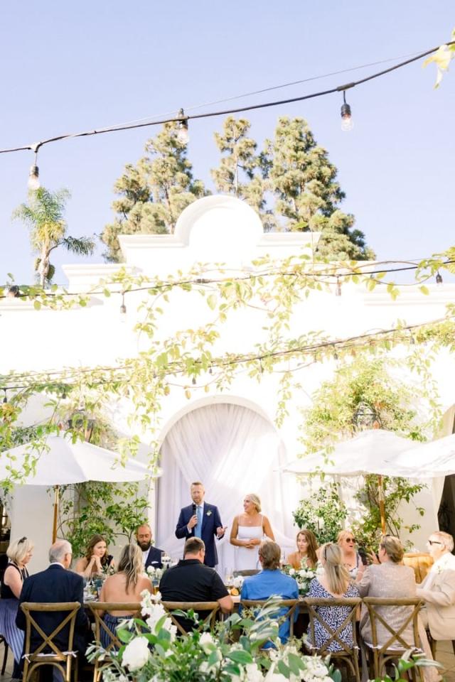 Bride and groom standing in courtyard with guests watching for Sara & James’ Wedding
