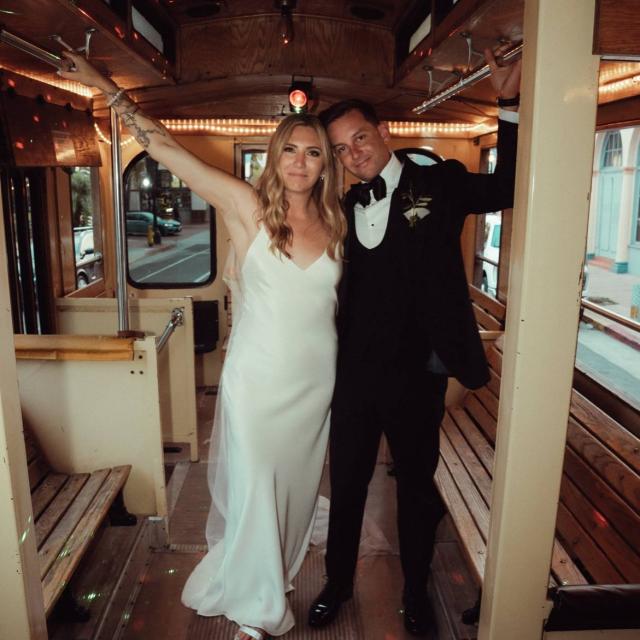 A bride and groom smile and pose inside a decorated trolley with wooden seats.